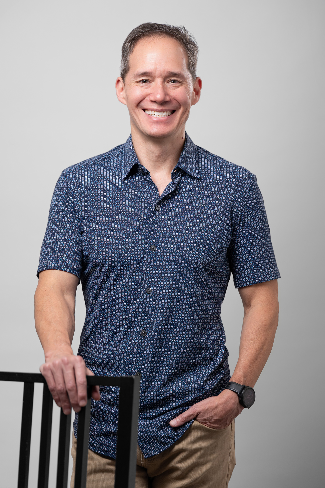 Edward Chu wearing a blue button up shirt with one hand on a chair